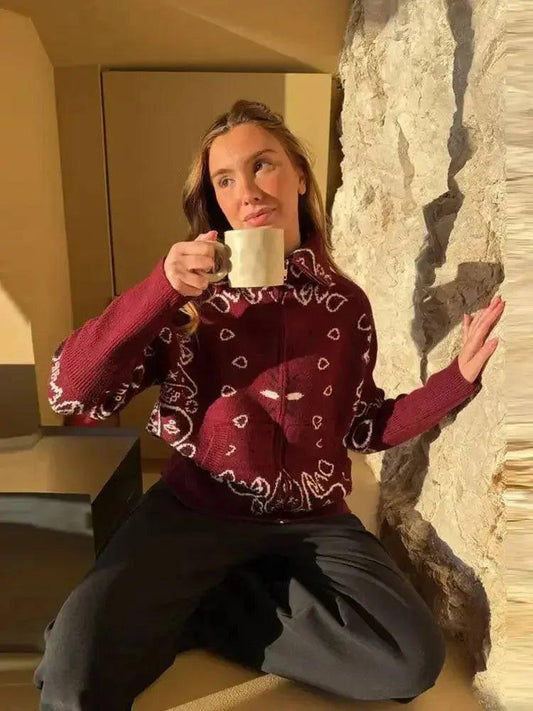 Woman in maroon bandana print sweater holding coffee mug, cozy indoor fashion look