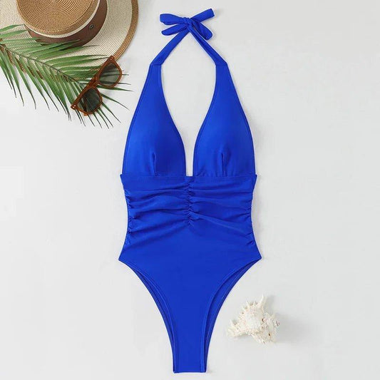 Blue halter one-piece swimsuit with ruched waist, beach hat, sunglasses, and palm leaf