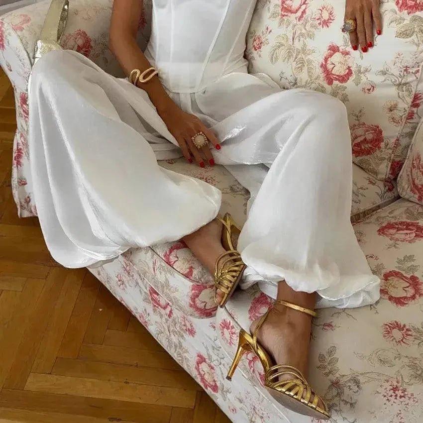 Woman in white satin wide-leg pants and gold heels on floral couch, fashion outfit