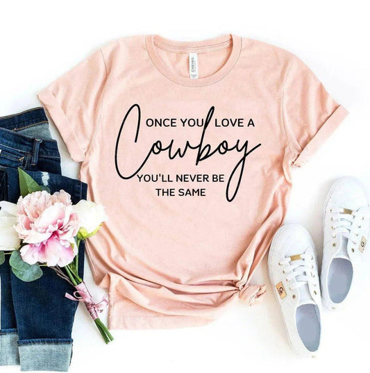 Pink graphic tee with 'Once You Love a Cowboy' text, paired with jeans, white sneakers, and pink flowers