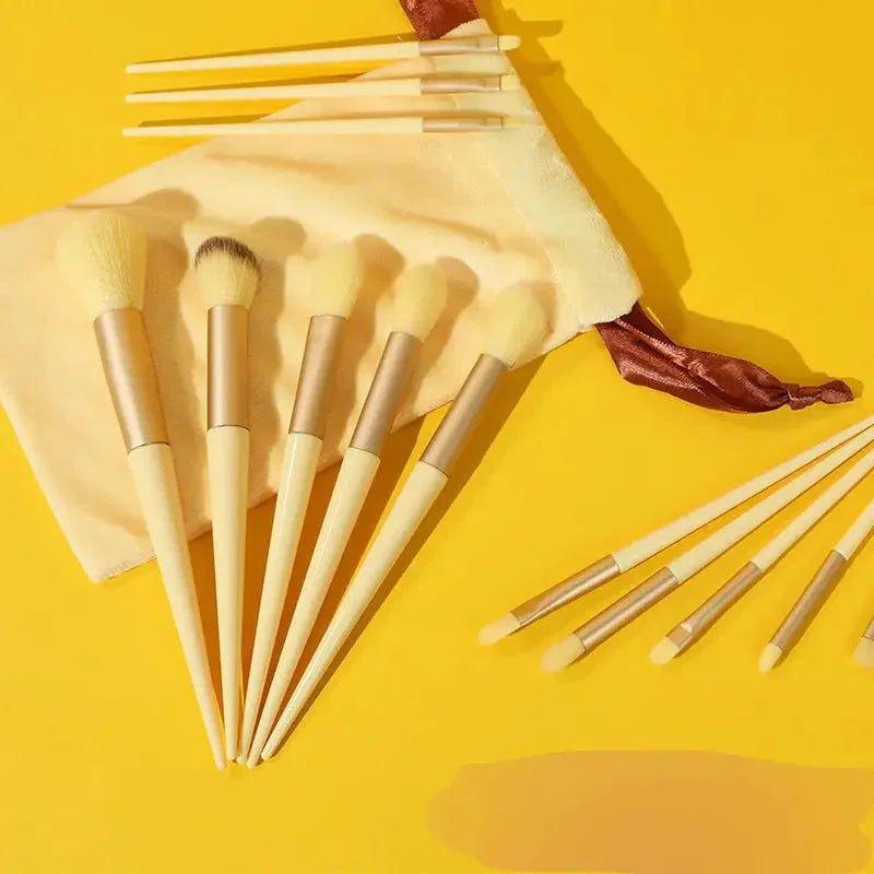 Luxury makeup brushes set with gold accents, cream handles, and velvet pouch on vibrant yellow background