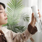 Woman using facial mist spray for skincare, beauty routine with green leaf backdrop