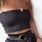 Black crop top with thin straps, layered gold necklaces, and high-waist pants with belt