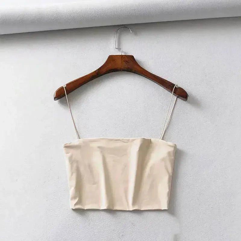 Beige women's crop top with thin straps on wooden hanger, minimalist fashion style