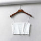 White women's crop top with thin straps on wooden hanger, minimalist fashion style