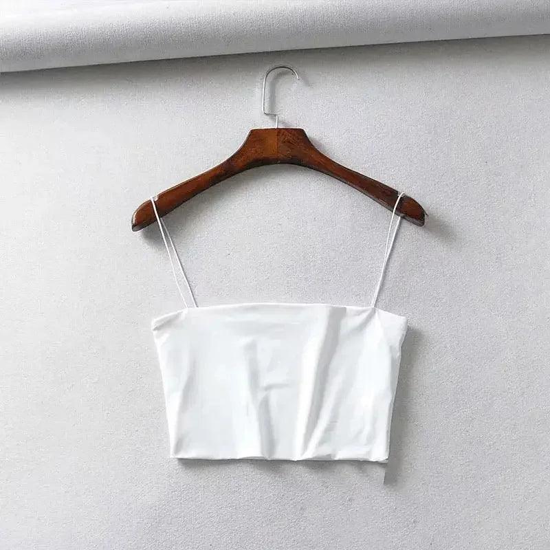 White women's crop top with thin straps on wooden hanger, minimalist fashion style