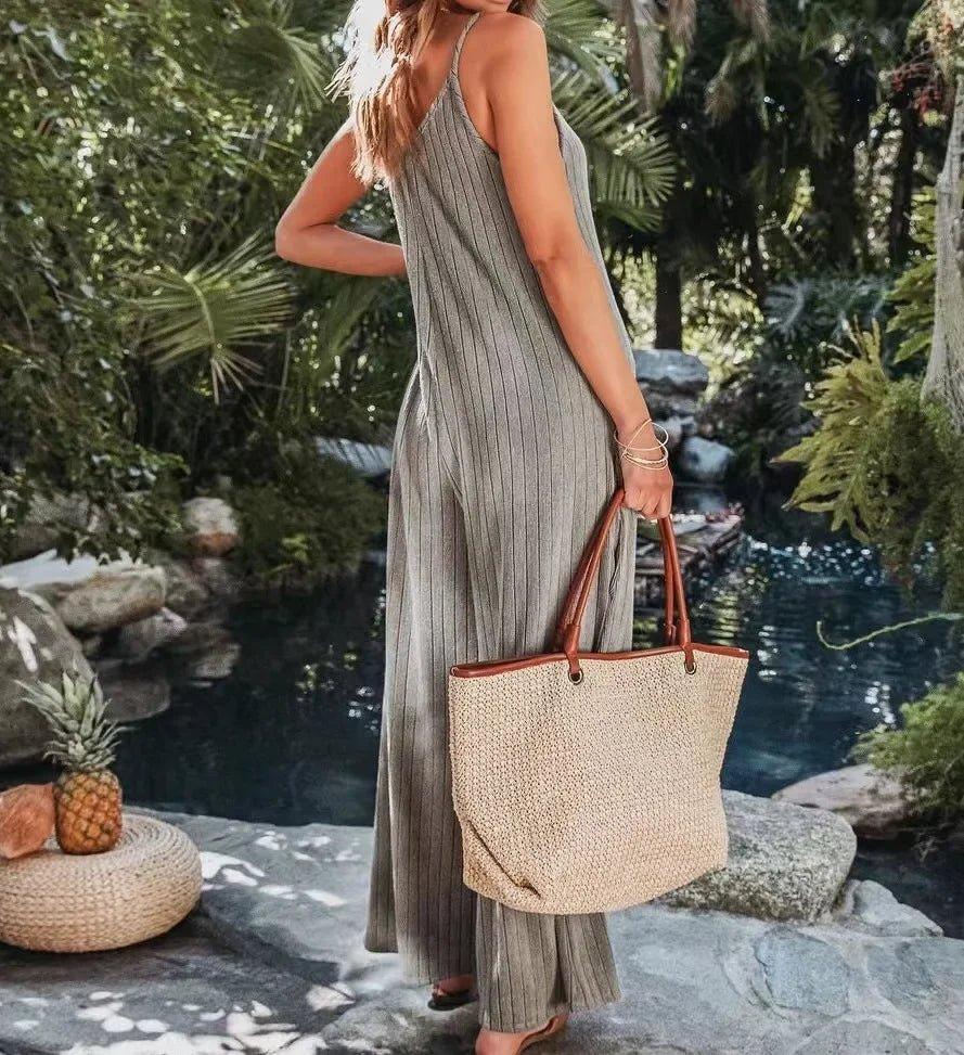Woman in striped jumpsuit holding woven tote bag by tropical pool, summer fashion outfit
