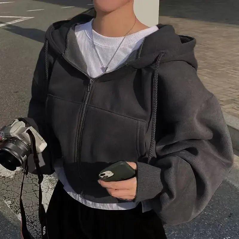 Woman wearing cozy gray zip-up hoodie with white tee, holding camera and phone, street style fashion