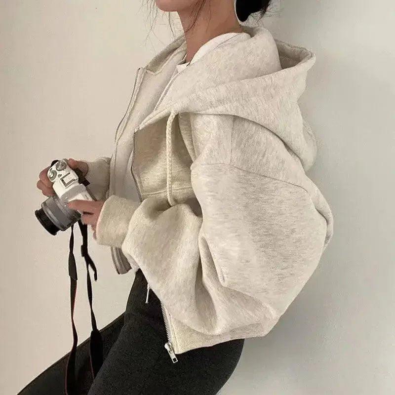 Woman in cozy beige zip-up hoodie holding camera, stylish streetwear fashion
