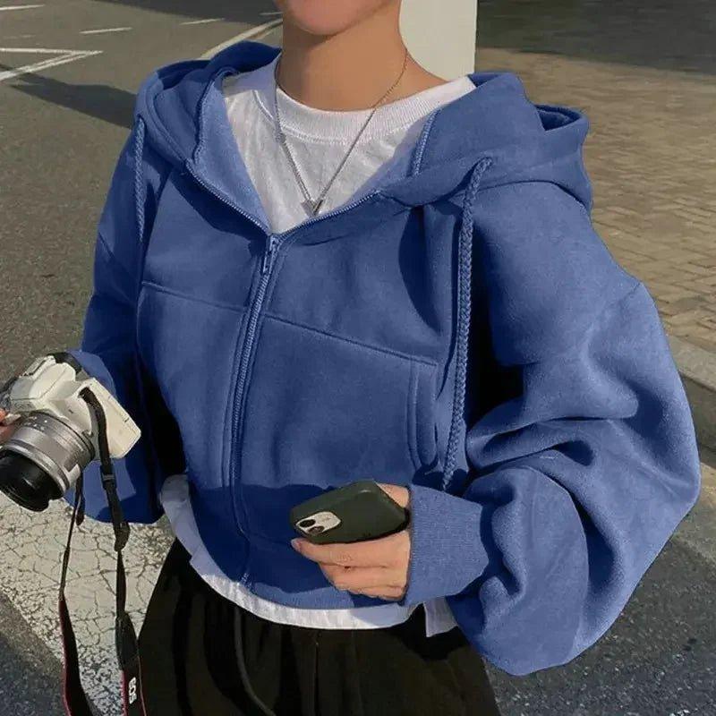 Woman wearing blue zip-up hoodie, holding camera and phone, street fashion style