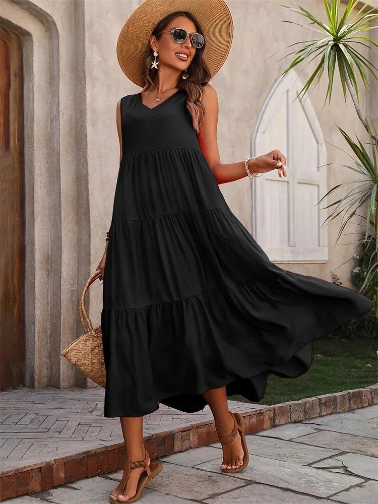 Woman in black tiered midi dress, straw hat, sunglasses, and woven bag, walking outdoors