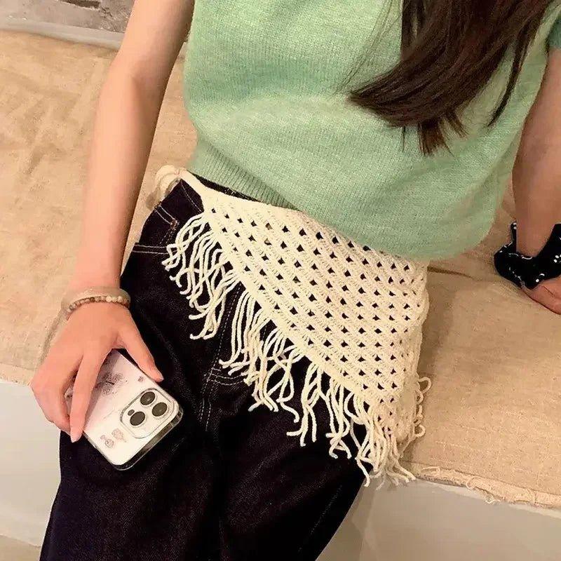 Woman wearing mint green top with cream crochet fringe belt, black jeans, holding phone