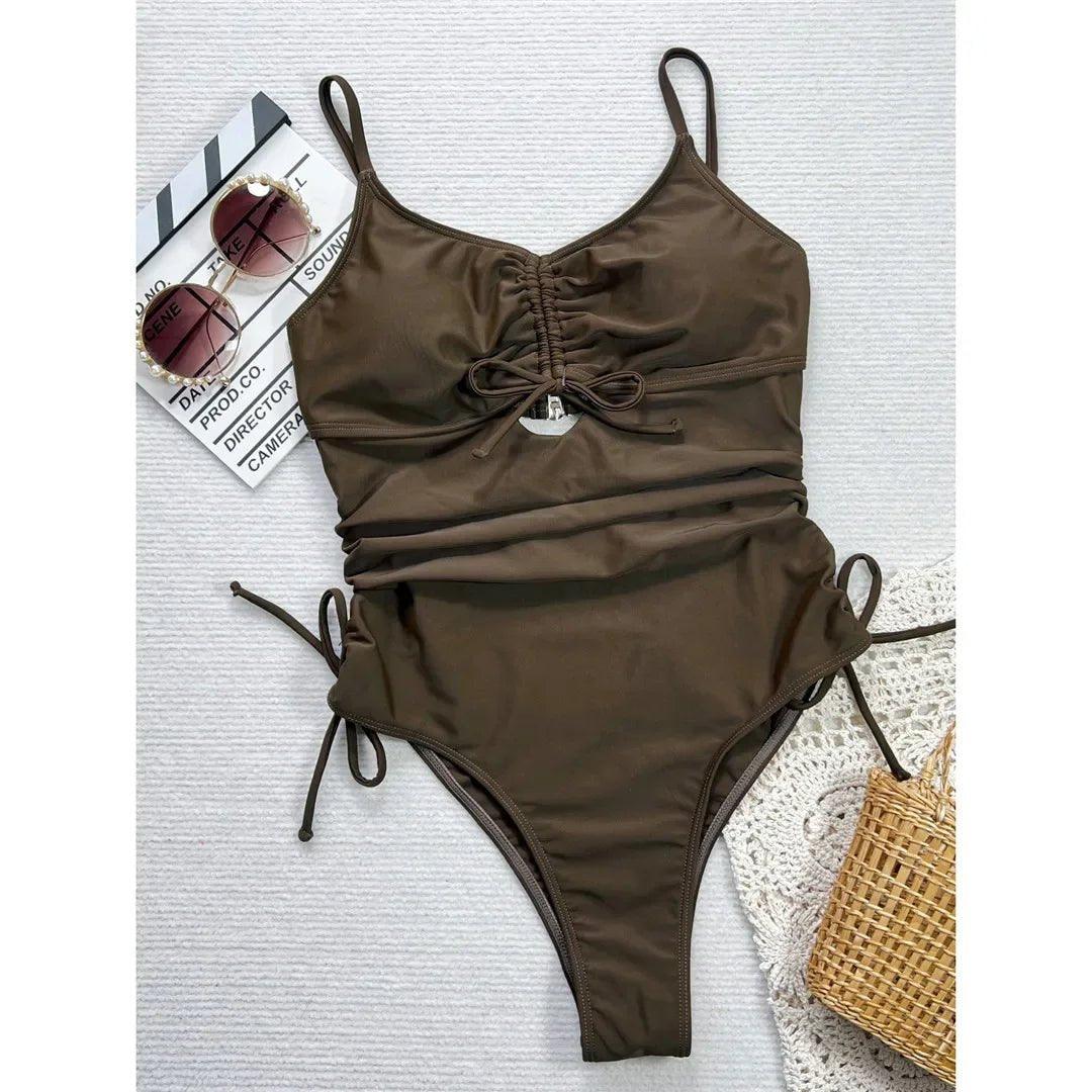 Olive green ruched one-piece swimsuit with side ties, sunglasses, and straw bag for women's beach fashion
