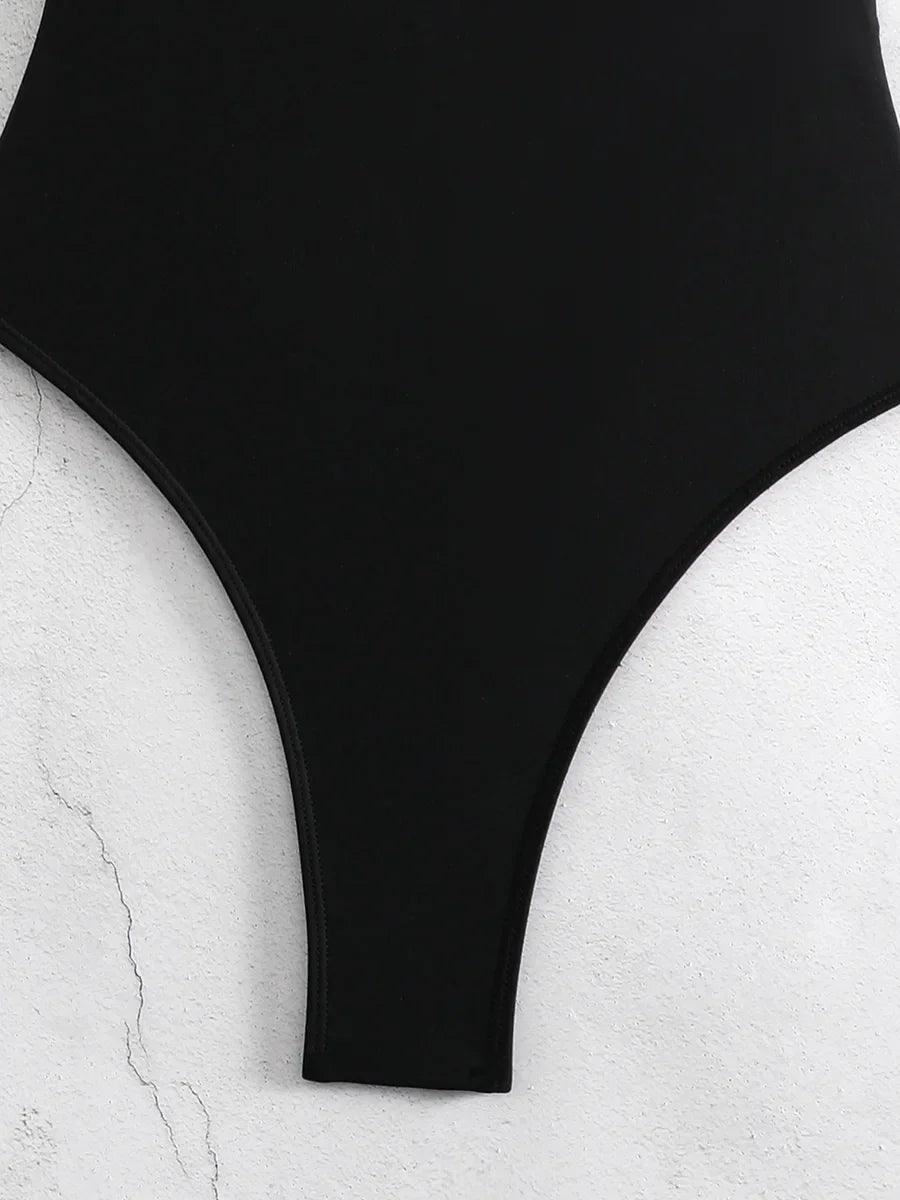Black high-cut one-piece swimsuit on textured white background, women's fashion