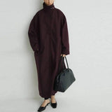 Woman in burgundy oversized coat with black bag and heels, modern fashion look