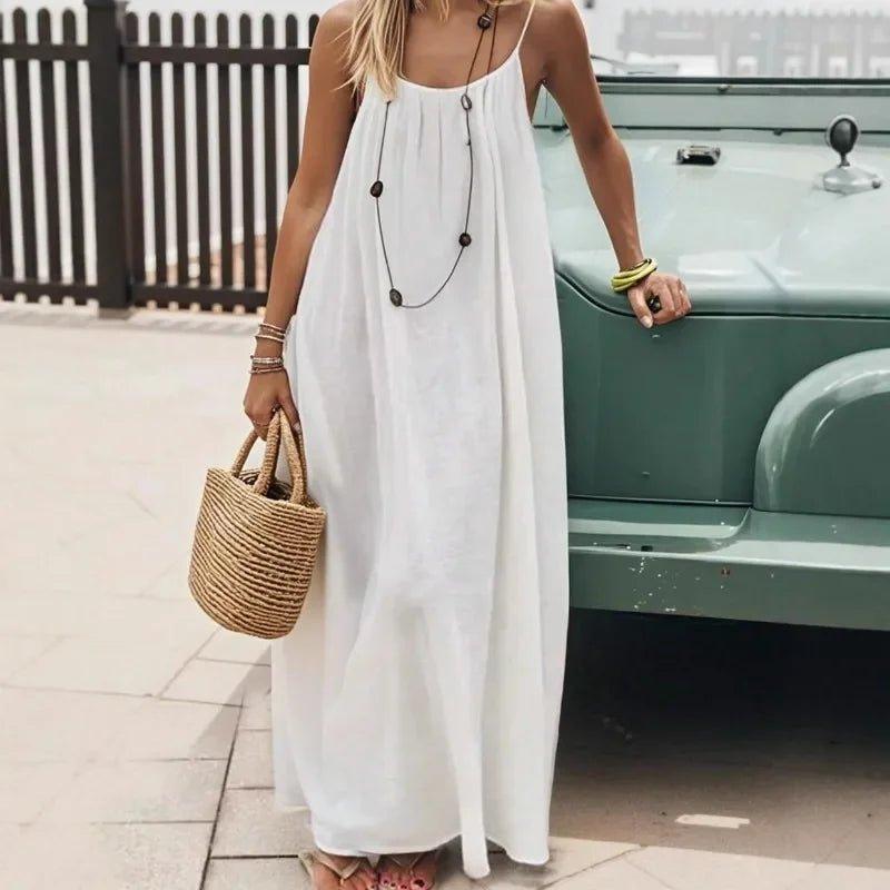 Woman in white boho maxi dress with straw bag, standing by vintage car, summer fashion style