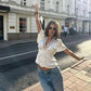 Woman in stylish white lace-trim blouse and jeans posing on city street, fashion outfit