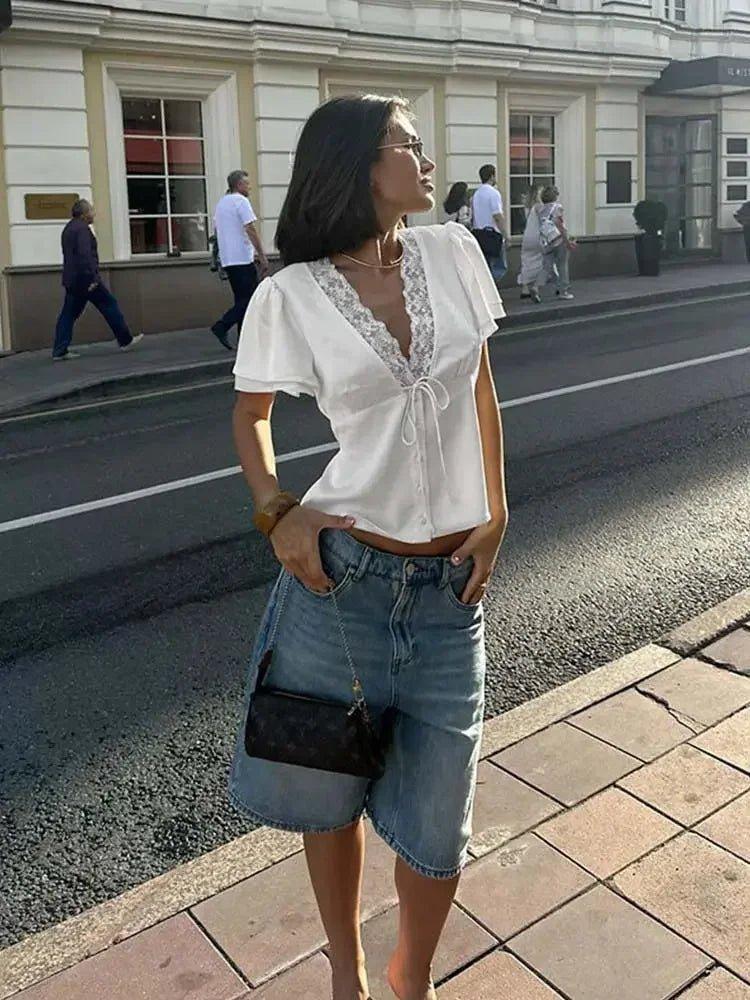 Woman in white lace-trim blouse and denim shorts, street style fashion
