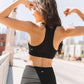 Woman in black sports bra and leggings flexing arms outdoors, fitness fashion