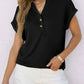 Woman wearing black button-front henley top with rolled sleeves, paired with white denim shorts for casual fashion.