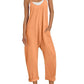 Woman in orange sleeveless jumpsuit with pockets, white sneakers, and straw hat for summer fashion