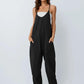 Woman wearing black sleeveless jumpsuit with pockets, paired with white top and sandals, stylish fashion outfit