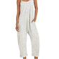 Woman in white textured jumpsuit with thin straps, straw hat, and white sneakers for casual summer fashion