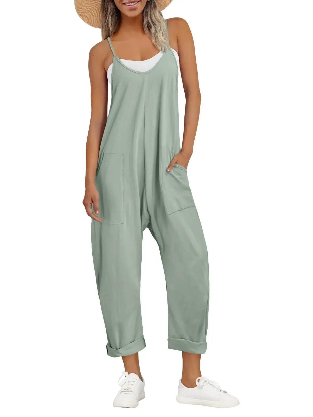 Woman in sage green sleeveless jumpsuit with pockets, white sneakers, and straw hat for casual fashion