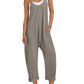 Woman in gray sleeveless jumpsuit with pockets, white sneakers, and straw hat for casual fashion