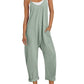 Woman in sage green sleeveless jumpsuit with pockets, white sneakers, and straw hat for summer fashion