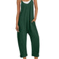 Green women's jumpsuit with pockets, white sneakers, and straw hat for casual fashion