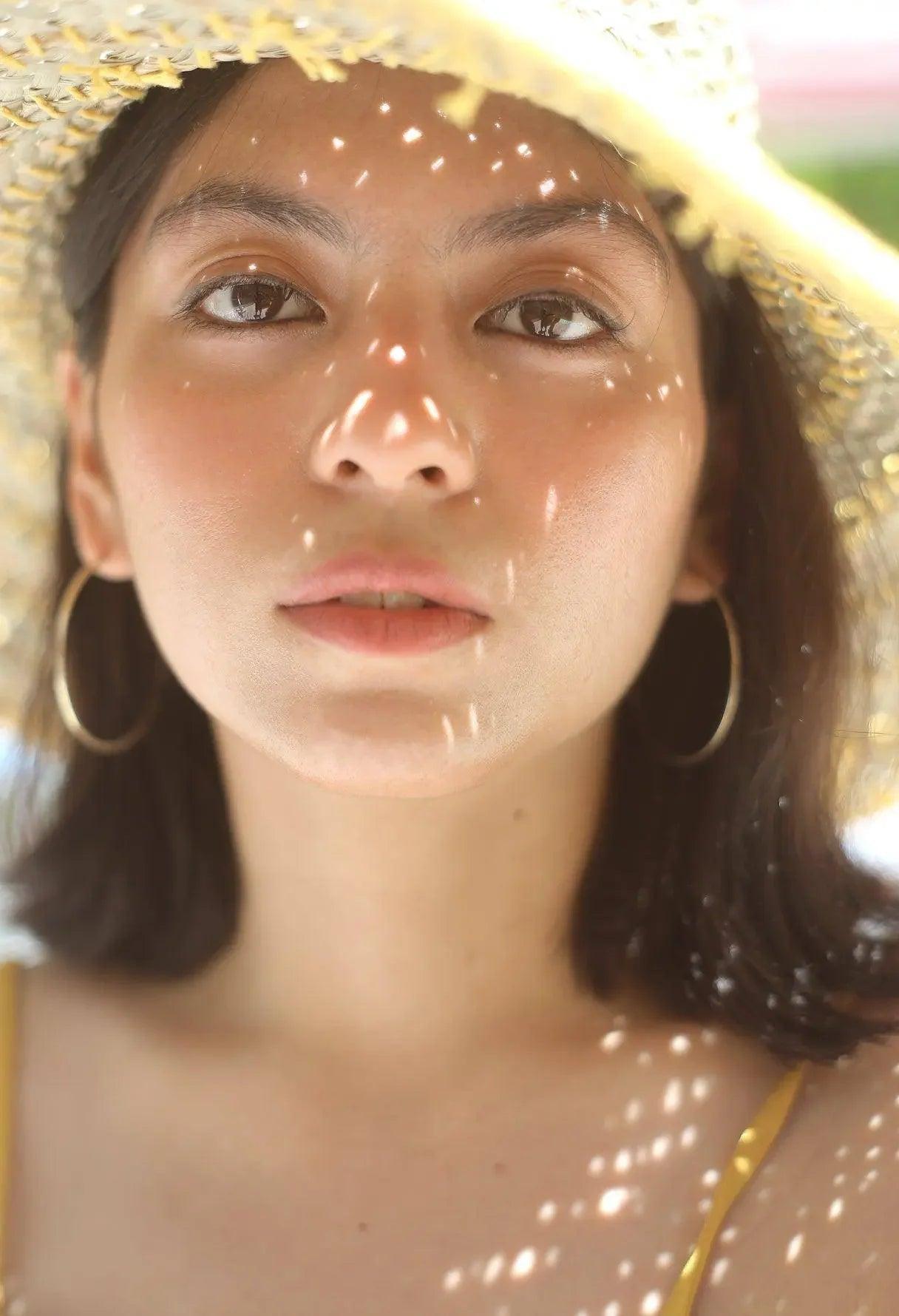 Woman in straw hat with glowing skin, gold hoop earrings, and summer vibes