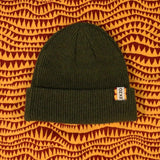 Olive green ribbed knit beanie with EKZO tag, styled on patterned fabric background