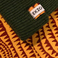 Green ribbed knit beanie with EKZO brand tag on patterned fabric background