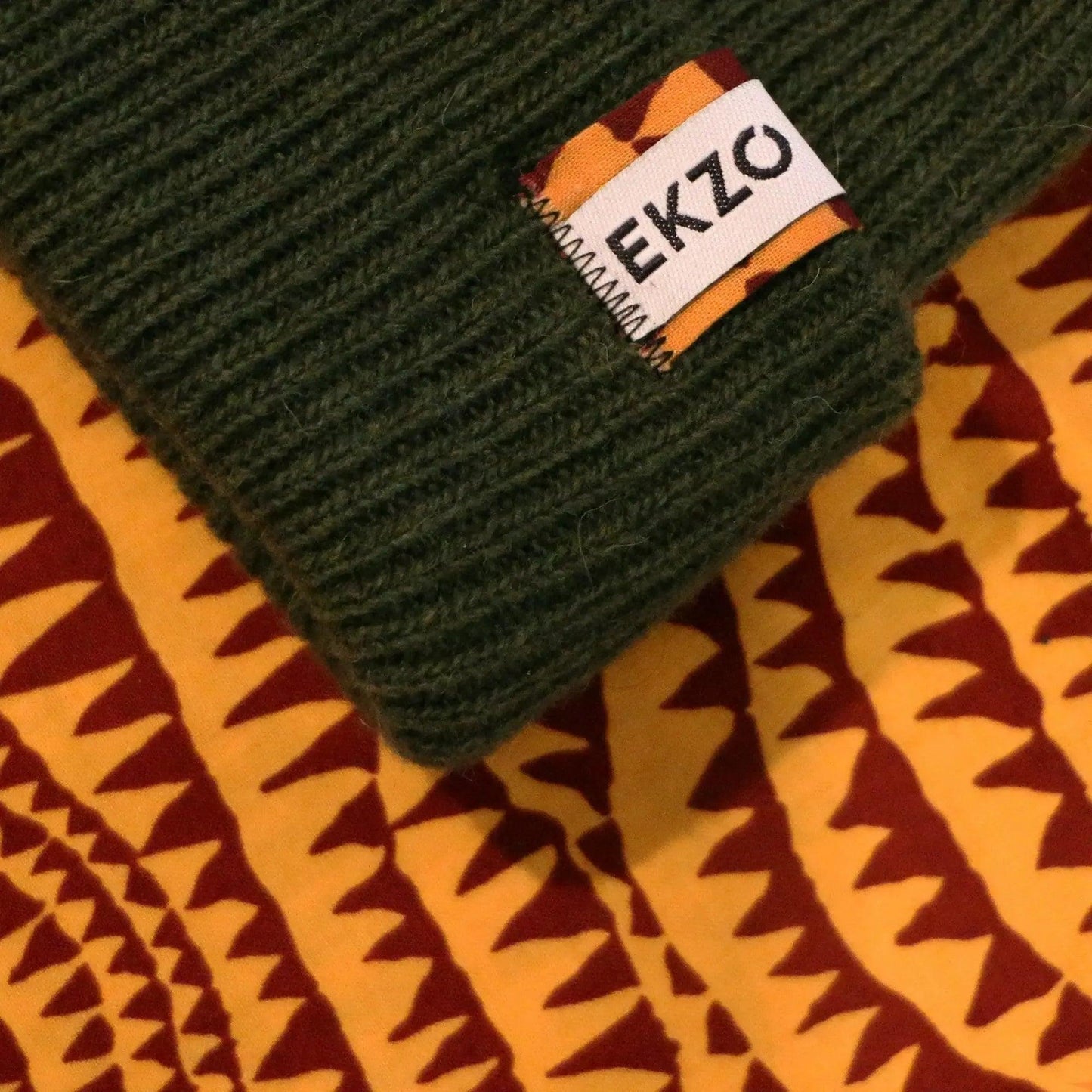 Green ribbed knit beanie with EKZO brand tag on patterned fabric background
