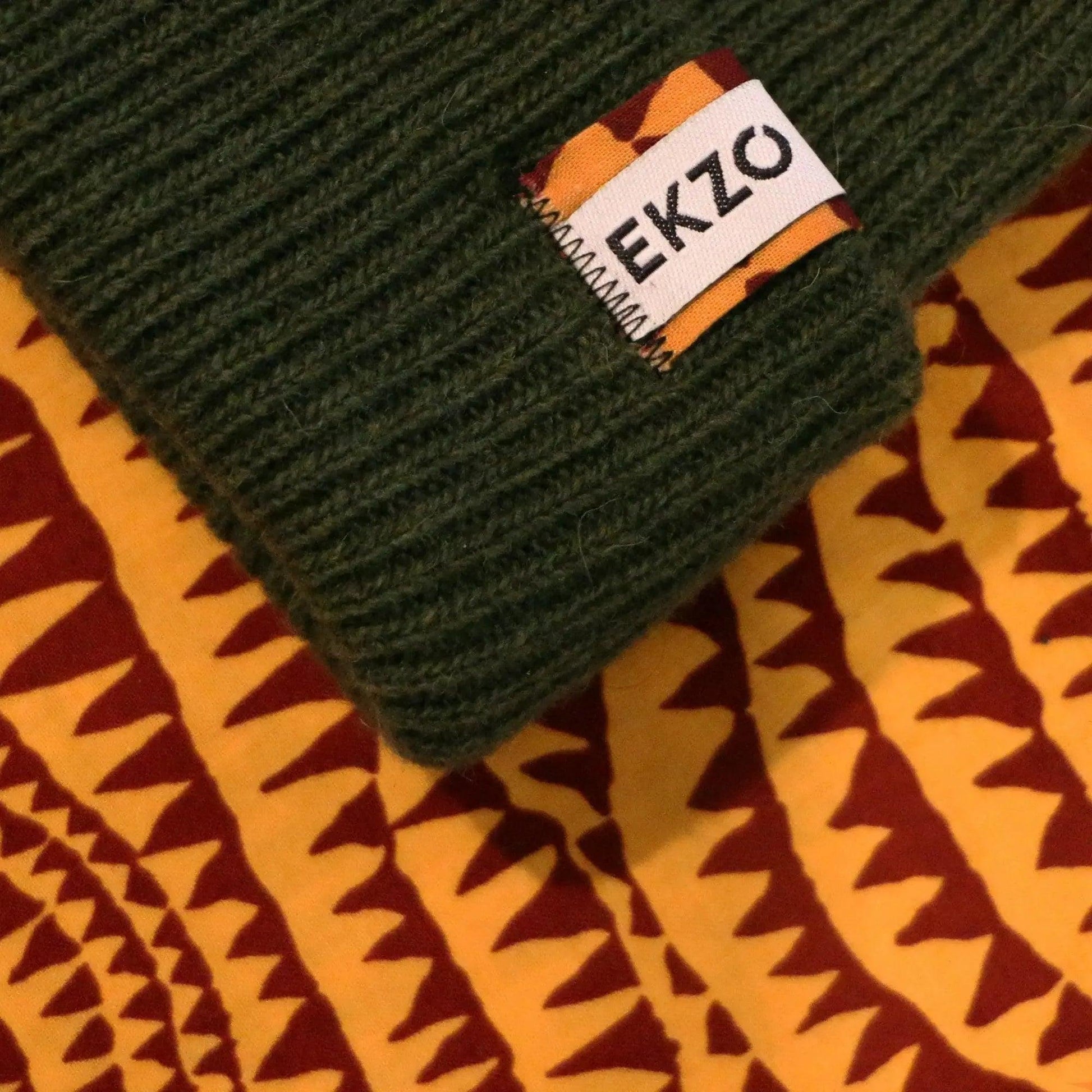 Green ribbed knit beanie with EKZO brand tag on patterned fabric background