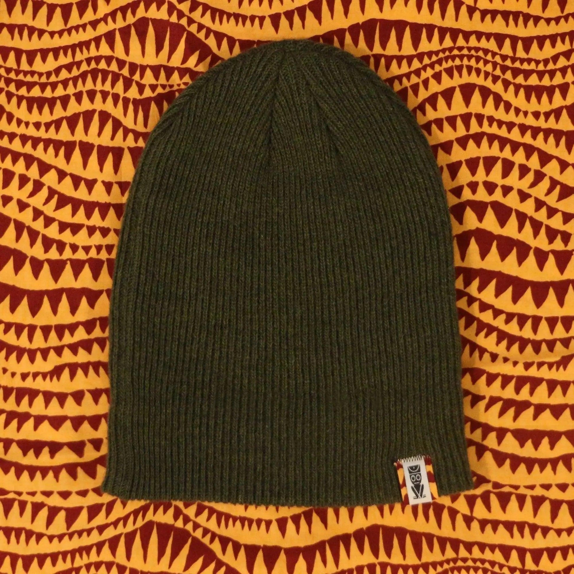 Olive green ribbed knit beanie with owl tag on patterned background, women's fashion accessory