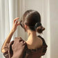 Woman in brown ruffle top with sleek bun hairstyle, elegant fashion look