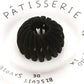 Black velvet hair scrunchie on white plate with Pâtisserie text, women's fashion accessory