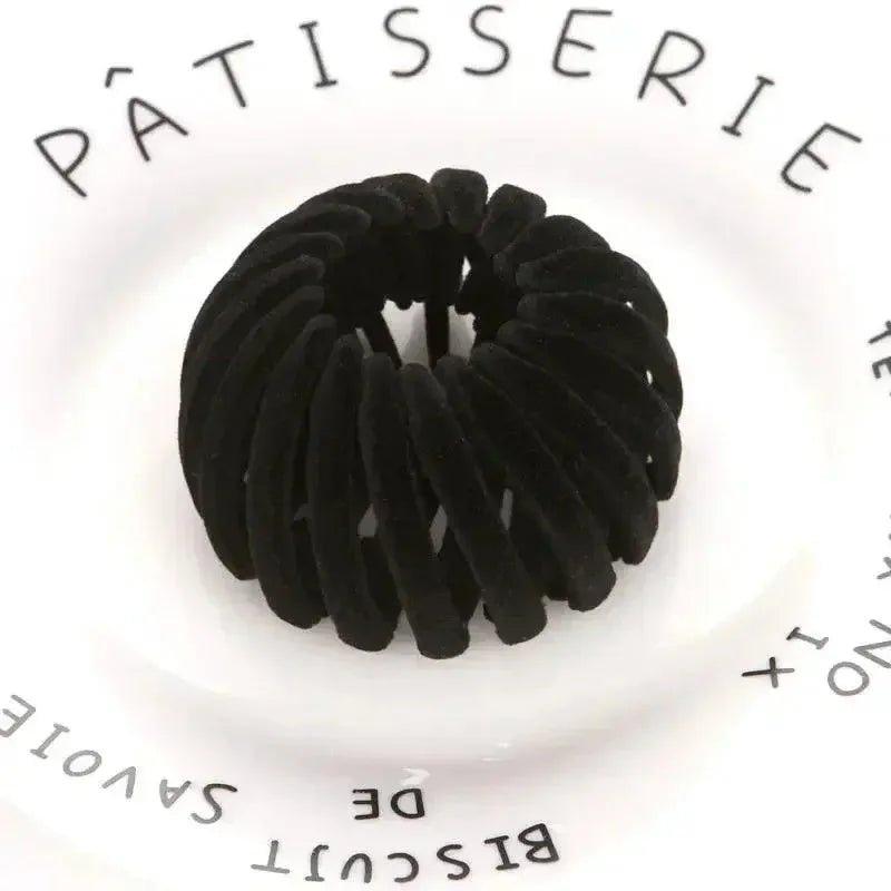 Black velvet hair scrunchie on white plate with Pâtisserie text, women's fashion accessory