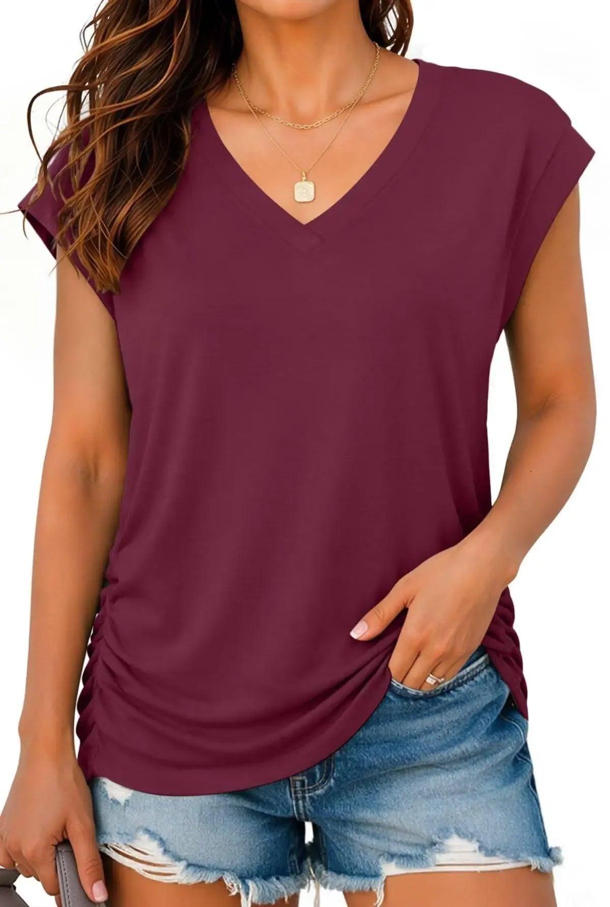Woman wearing burgundy V-neck short sleeve top with ruched side, paired with distressed denim shorts