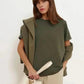 Woman in olive green oversized top with ruffled sleeves, beige pants, and white tote bag