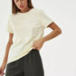 Woman modeling cream basic t-shirt with relaxed fit, paired with black pants for casual fashion look
