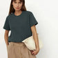 Woman in dark green t-shirt, beige pleated pants, holding white clutch bag — stylish casual fashion outfit