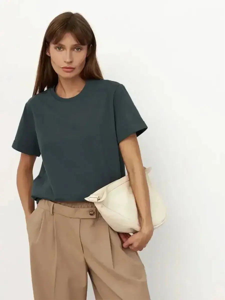 Woman in dark green t-shirt, beige pleated pants, holding white clutch bag — stylish casual fashion outfit