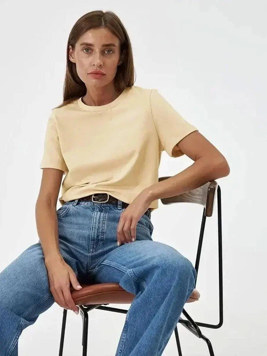 Woman in beige t-shirt and blue jeans sitting on chair, casual fashion outfit