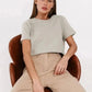 Woman in light gray crop top and beige wide-leg pants, seated on brown leather chair, fashion outfit