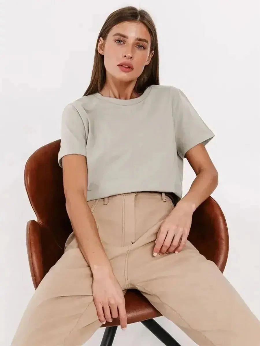 Woman in light gray crop top and beige wide-leg pants, seated on brown leather chair, fashion outfit