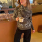 Woman in cozy gray bandana print hoodie with black pants, holding coffee mug at café