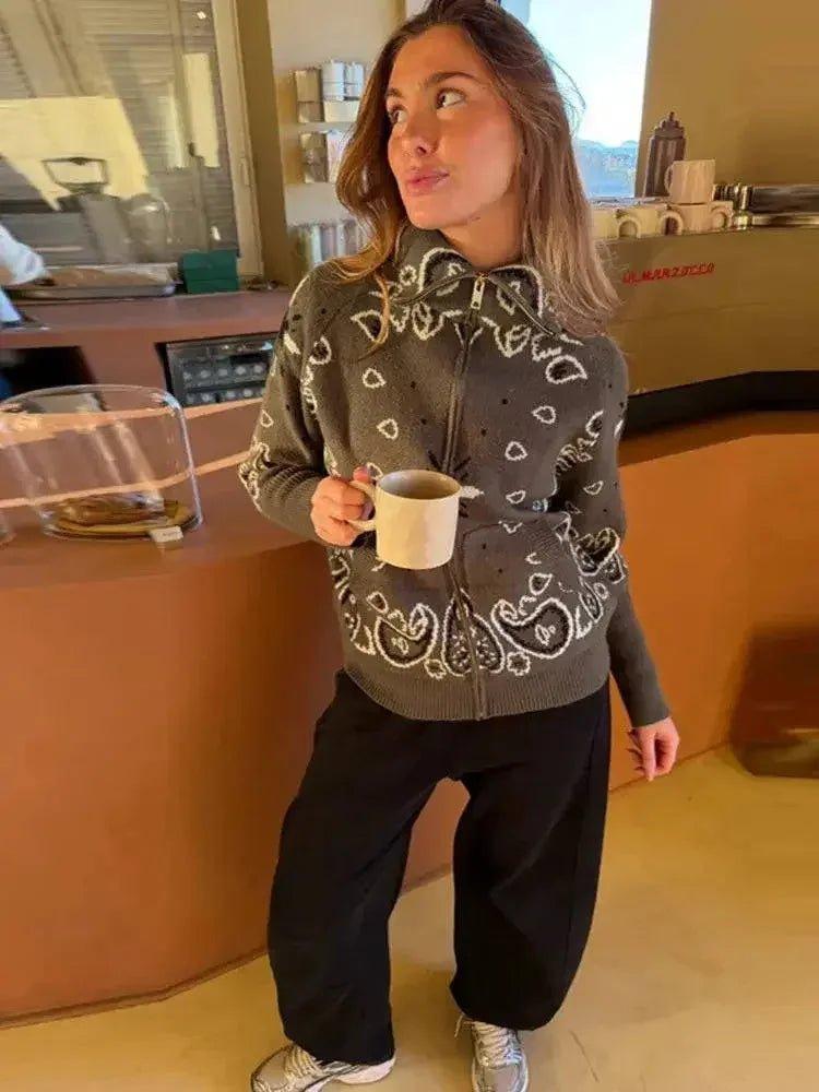 Woman in cozy gray bandana print hoodie with black pants, holding coffee mug at café